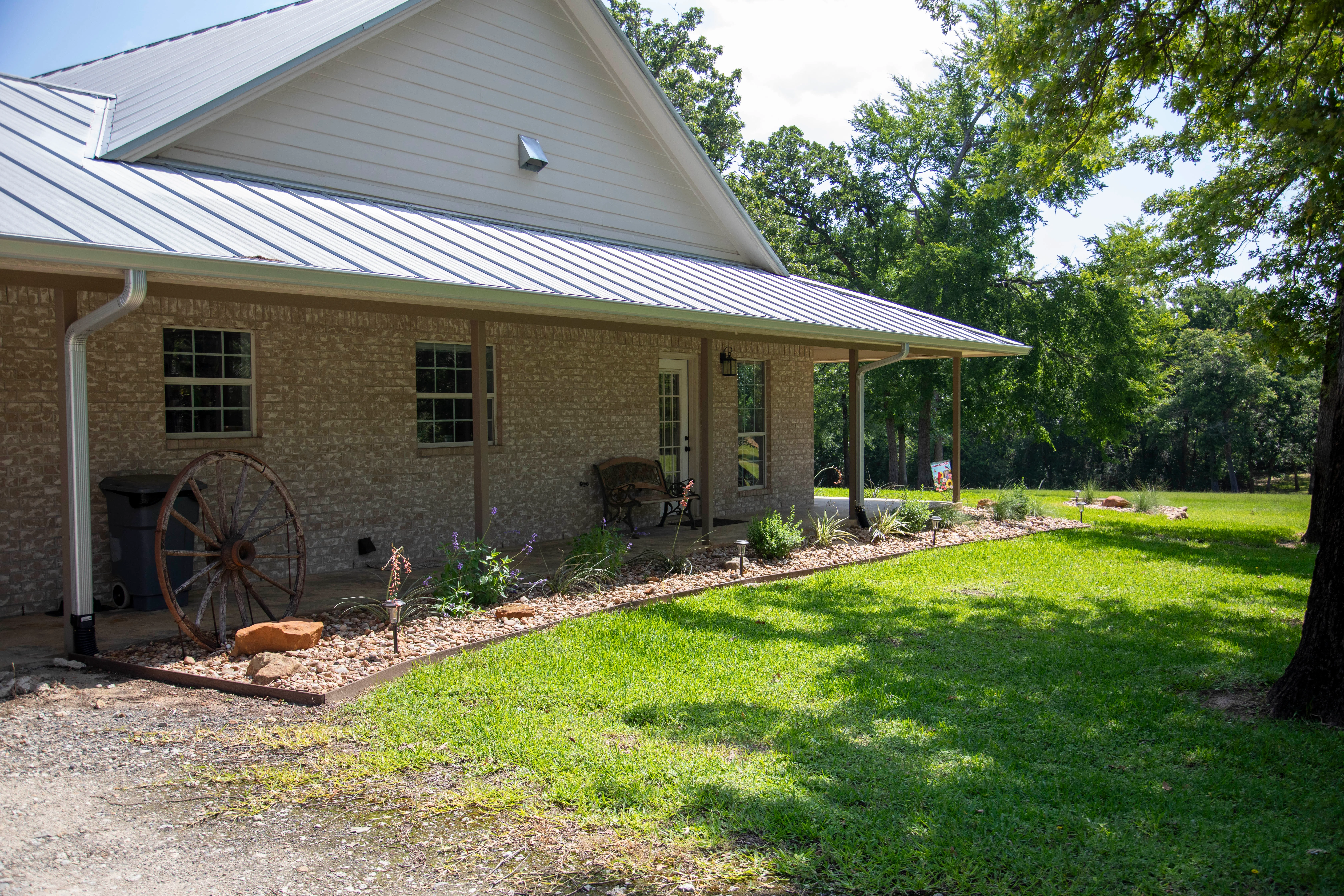 Brick home with metal roof, front porch, and landscaped gravel beds with plants
