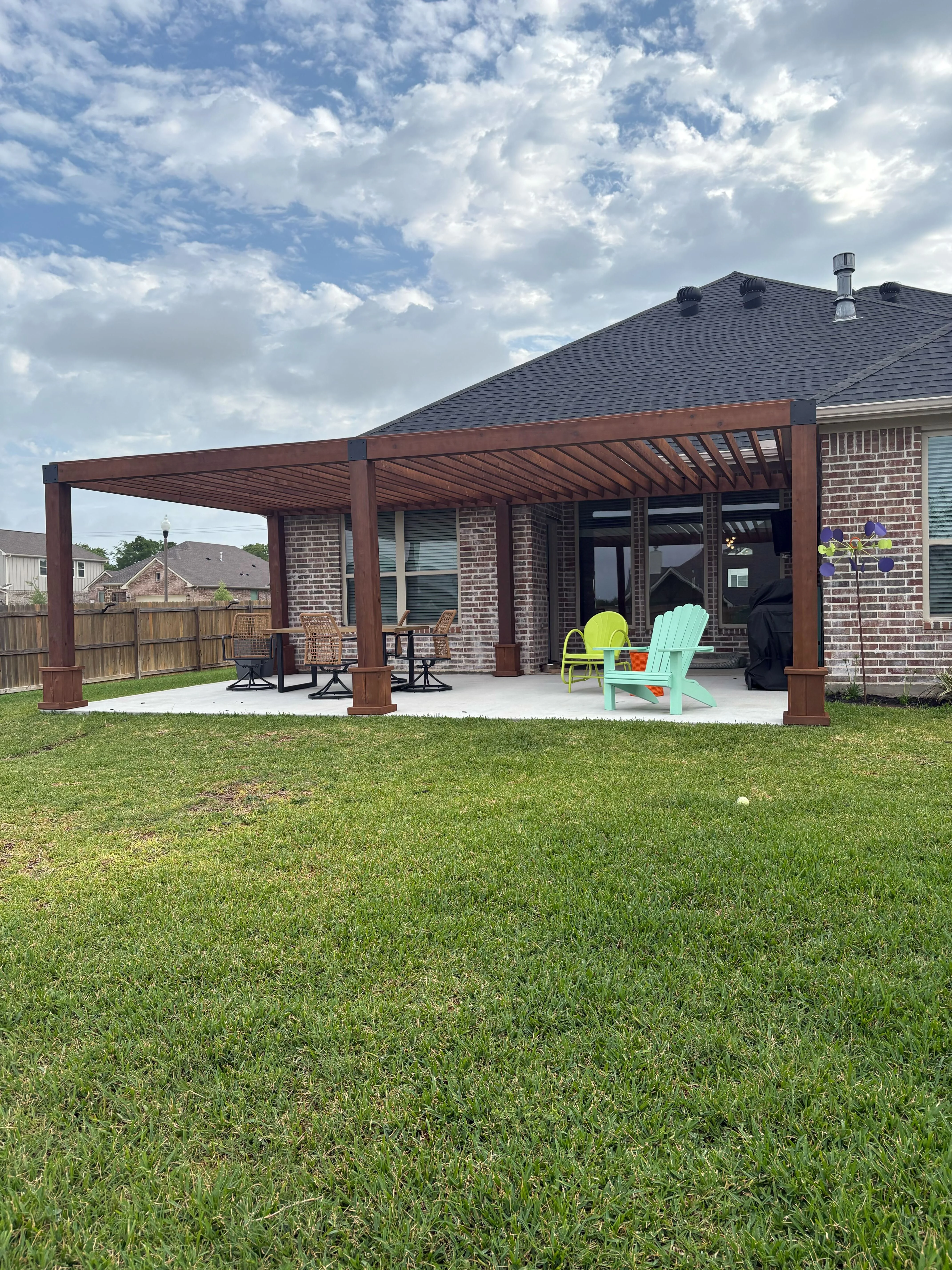 Brown wood pergola with louvered roof over concrete patio with green lawn and seating