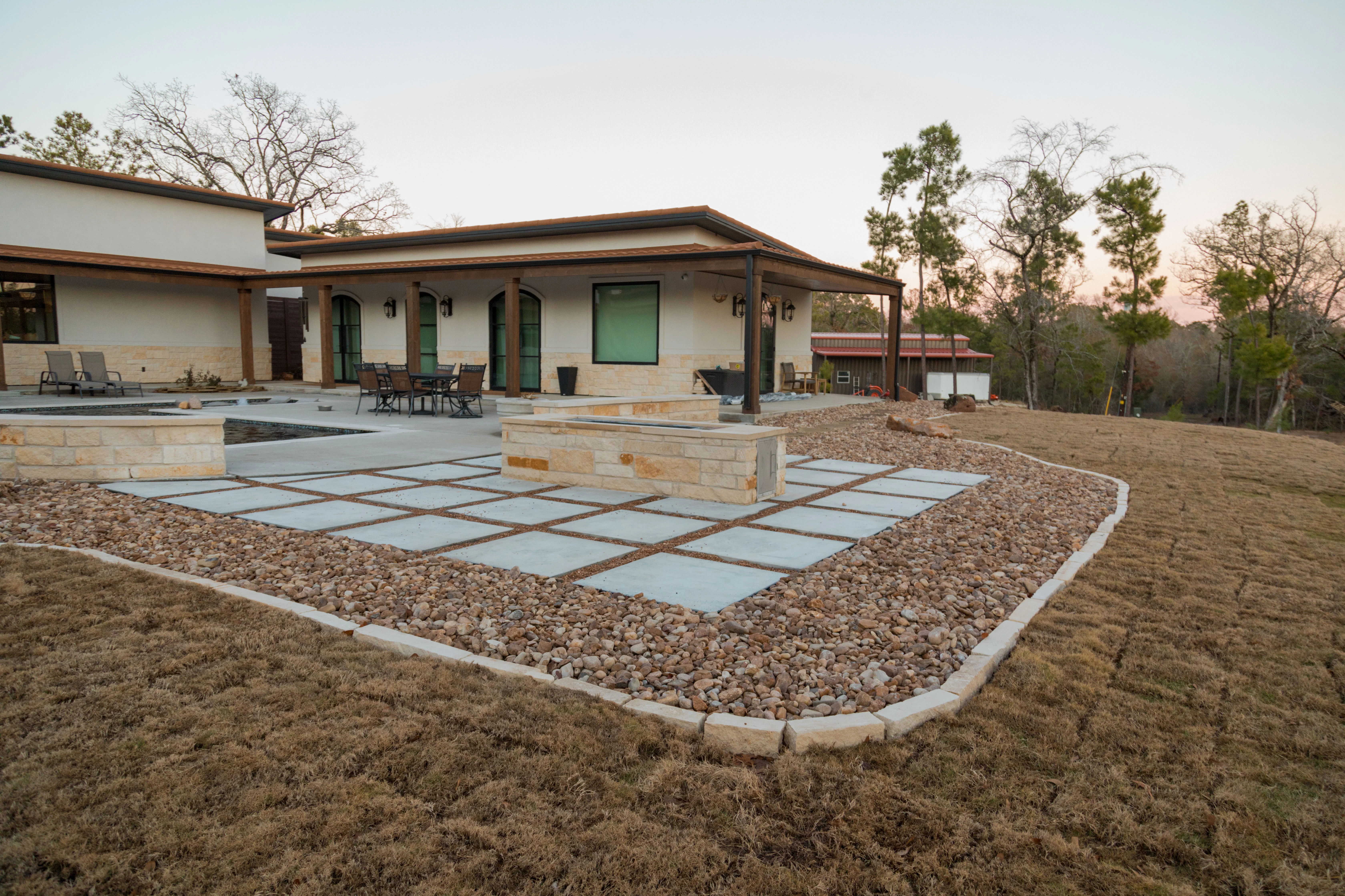Modern patio with concrete pavers, river rock borders, and steel edging — Hardscape Contractor by Landscaping Ninjas in College Station, TX