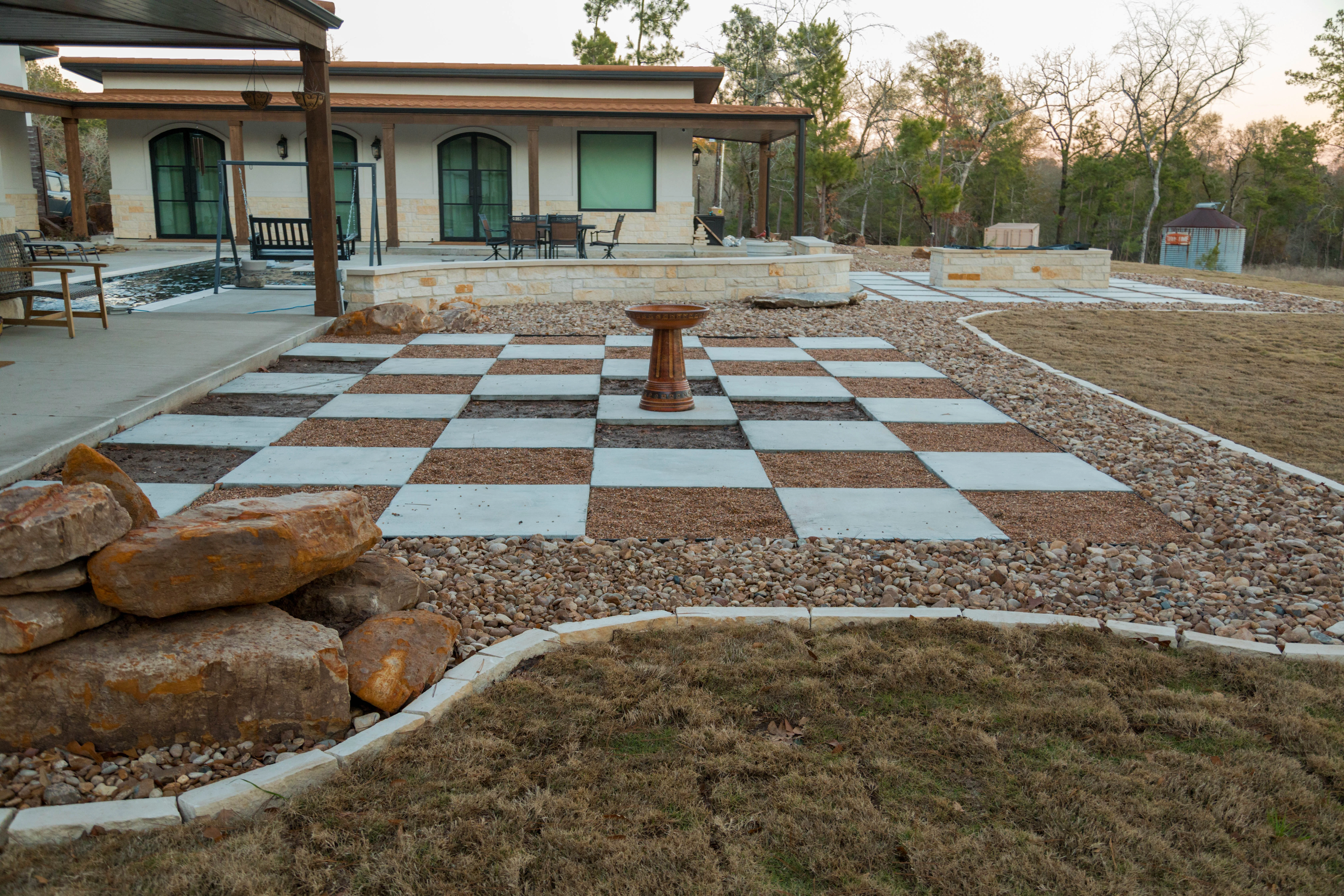 Checkerboard hardscape with concrete pavers, gravel, and central pedestal in residential landscape