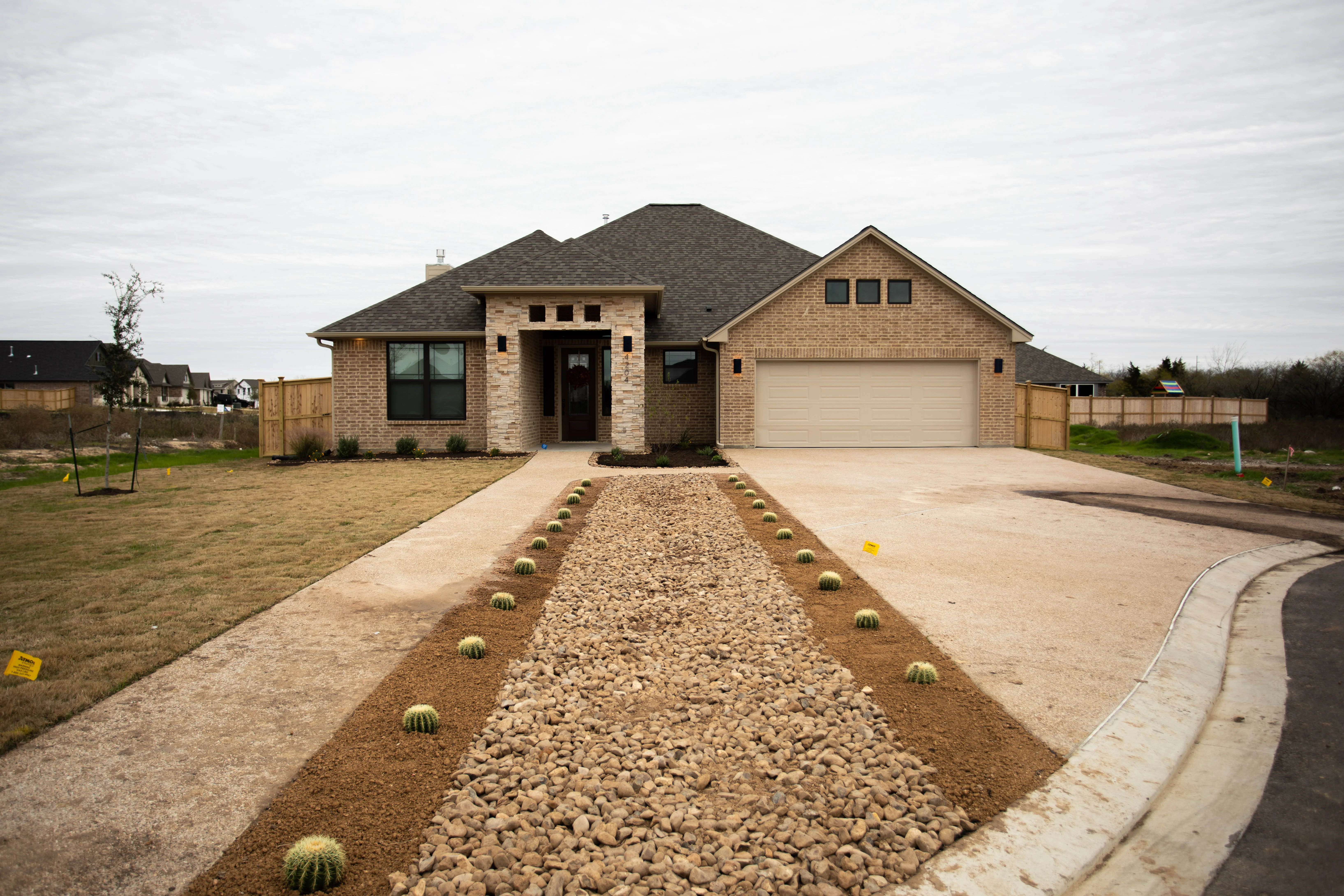 New brick home with gravel driveway lined with barrel cacti and concrete walkway