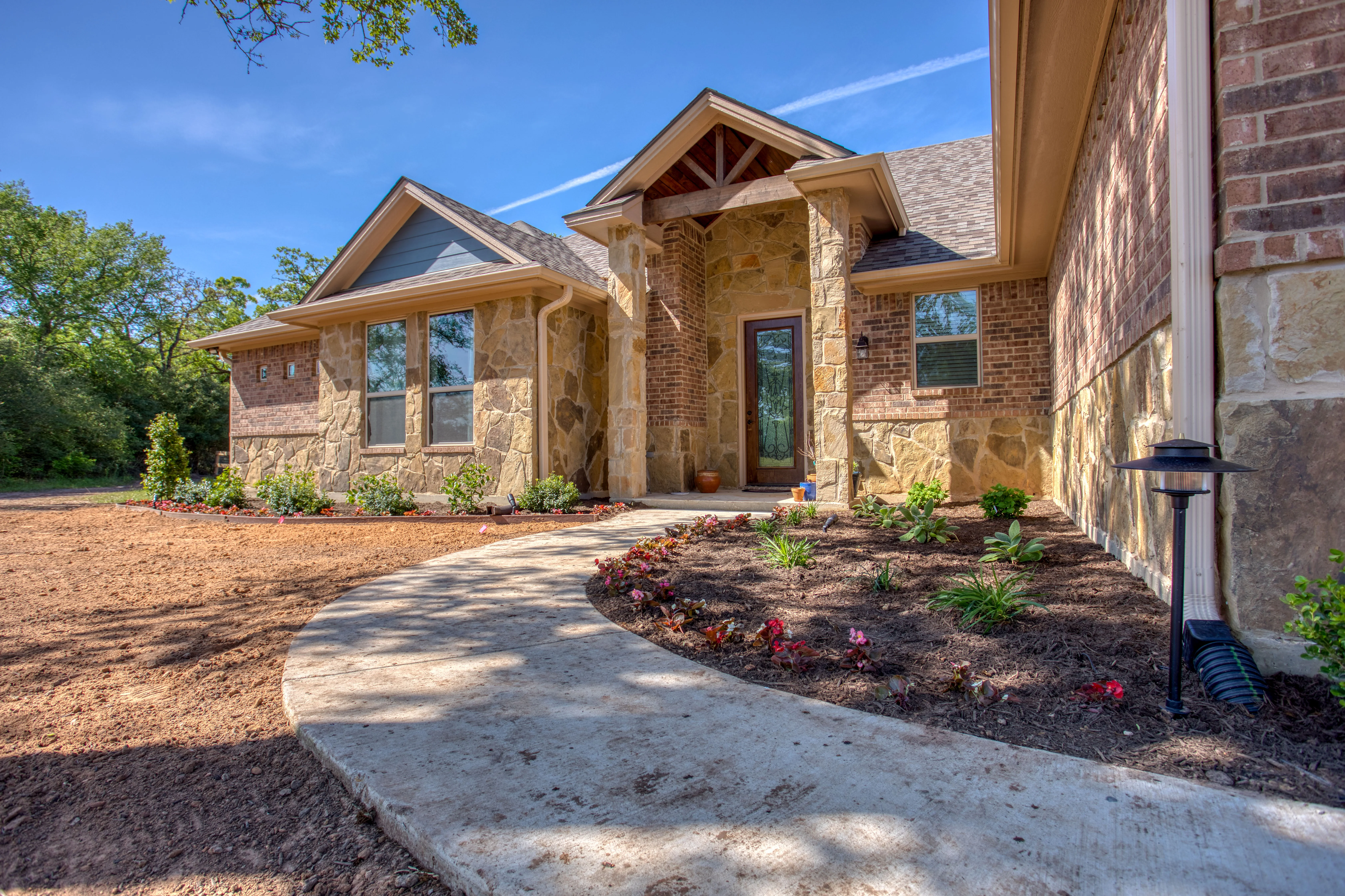 Modern stone and brick home with newly installed landscape beds and curved concrete walkway