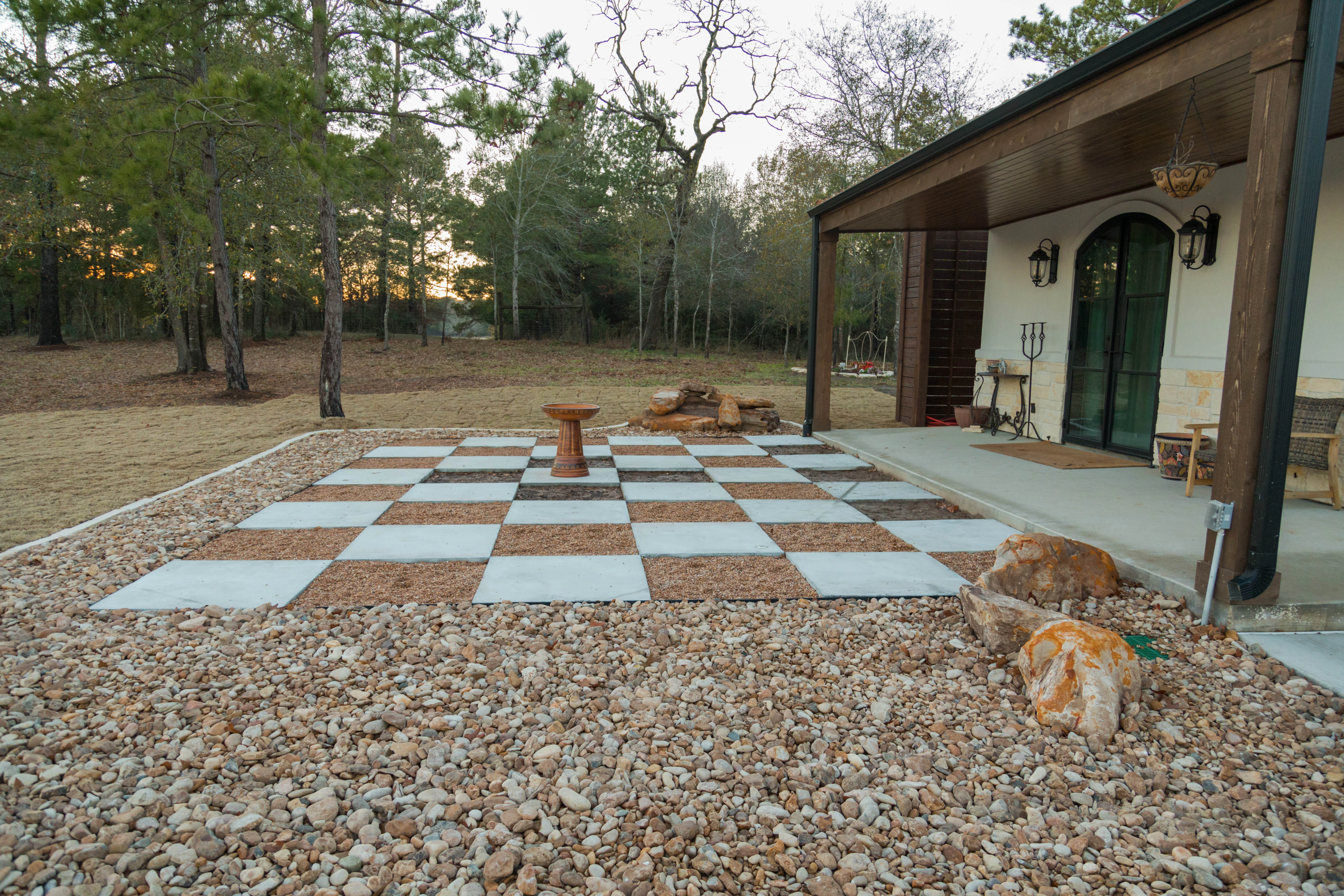 Checkerboard patio with concrete and gravel squares in wooded backyard setting
