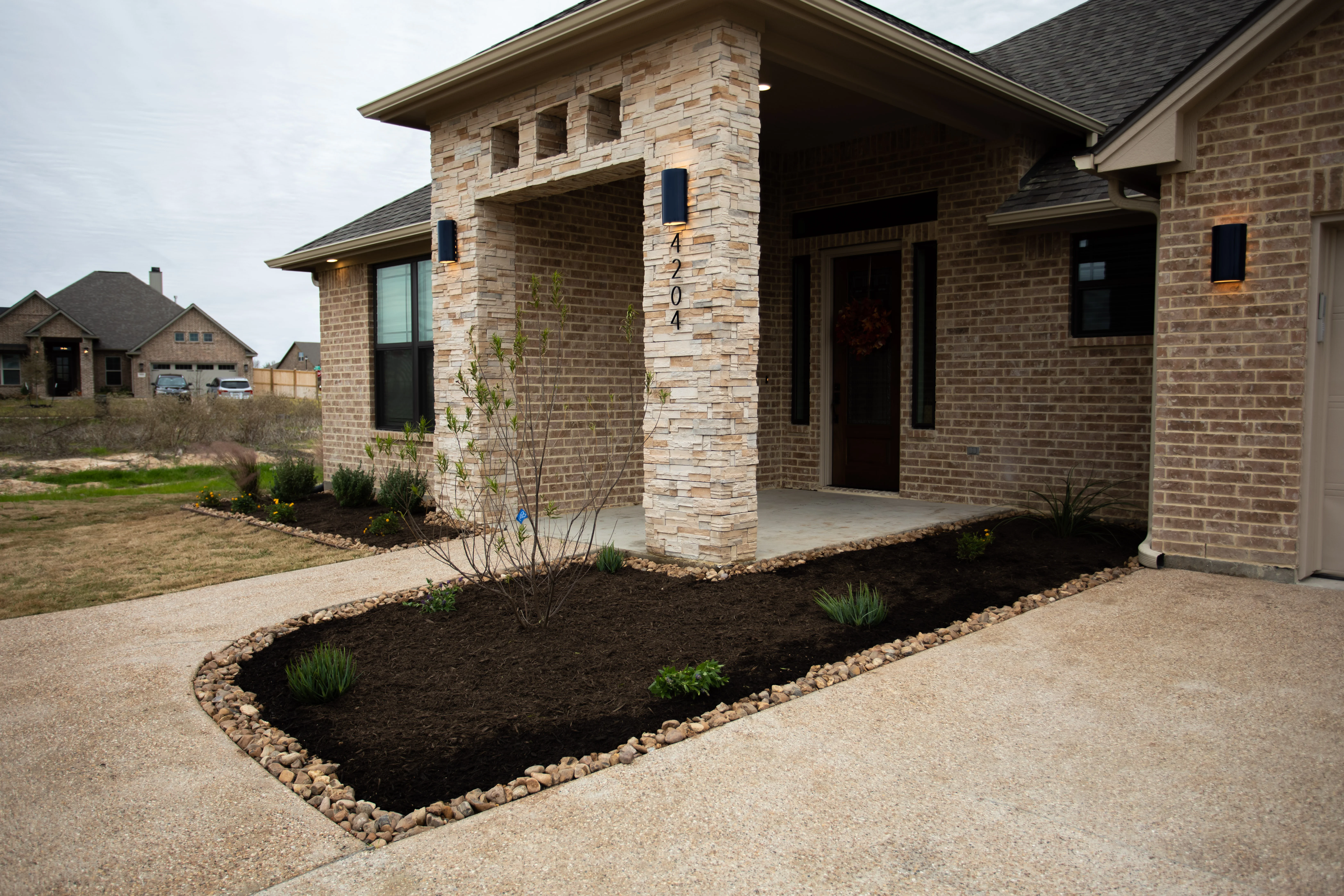 Front yard landscape with mulch beds, river rock borders, and new plantings at brick home