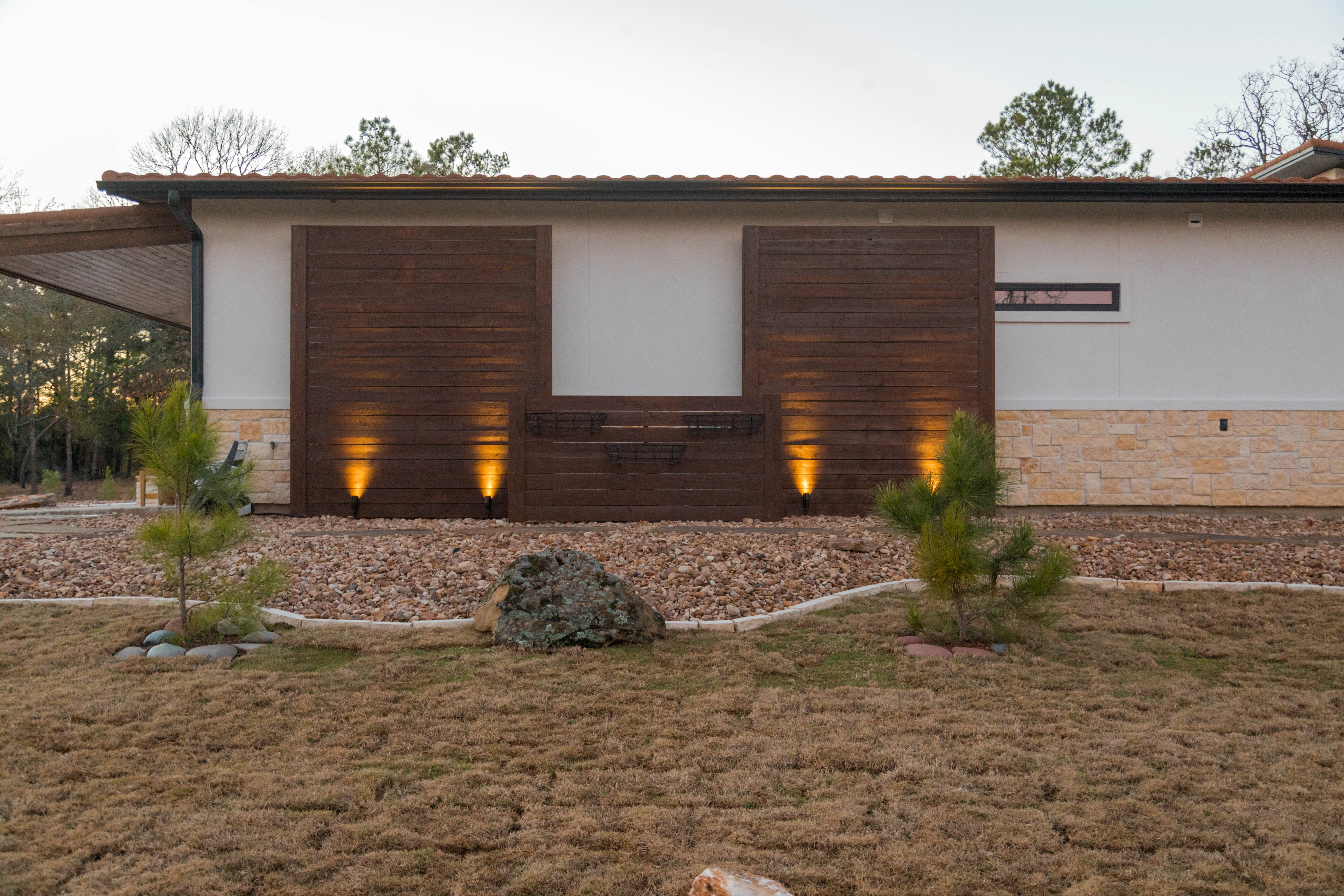 Modern home with gravel landscape, uplighting, and ornamental plants in College Station