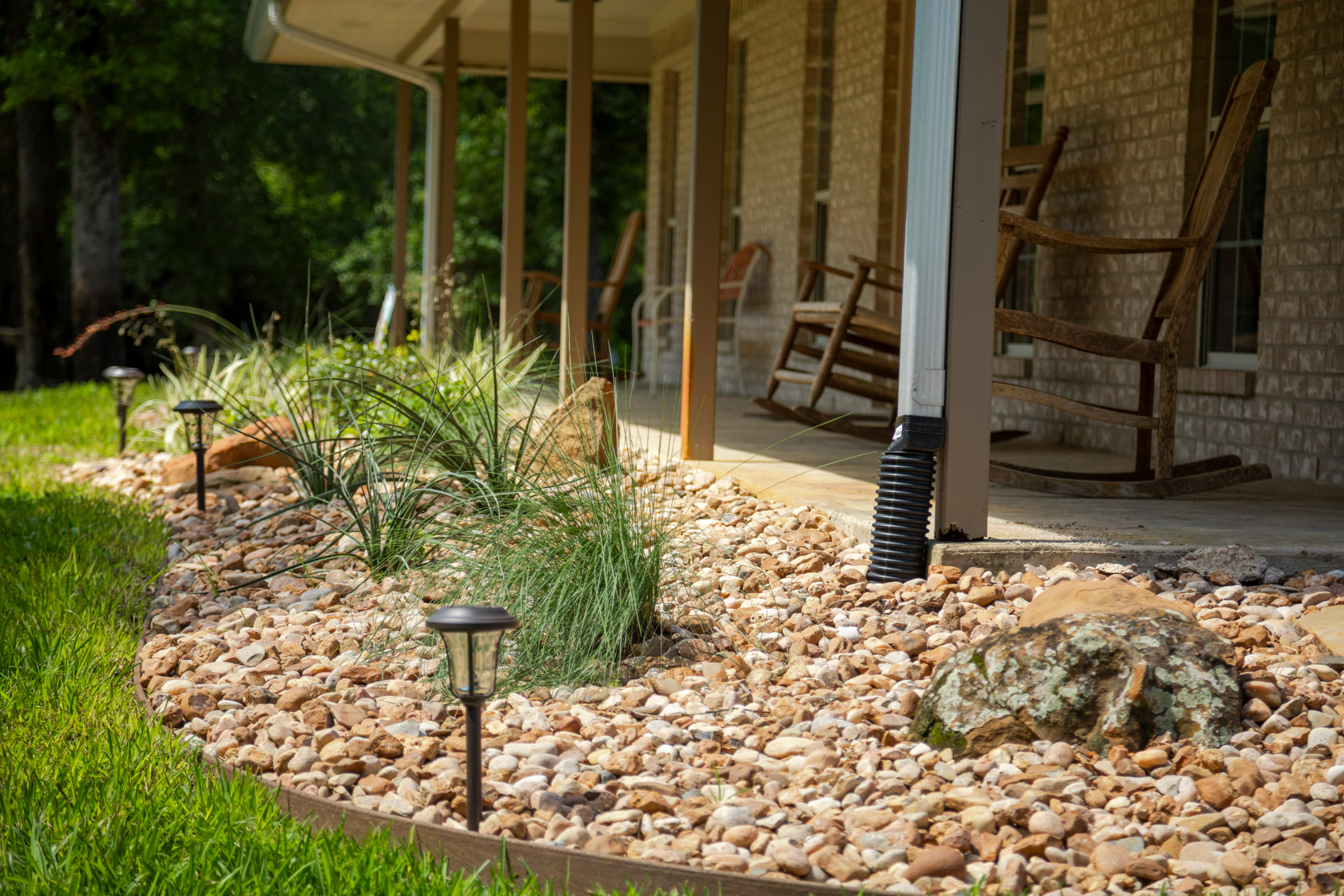 Decorative stone landscape bed with ornamental grasses and solar lights beside brick patio