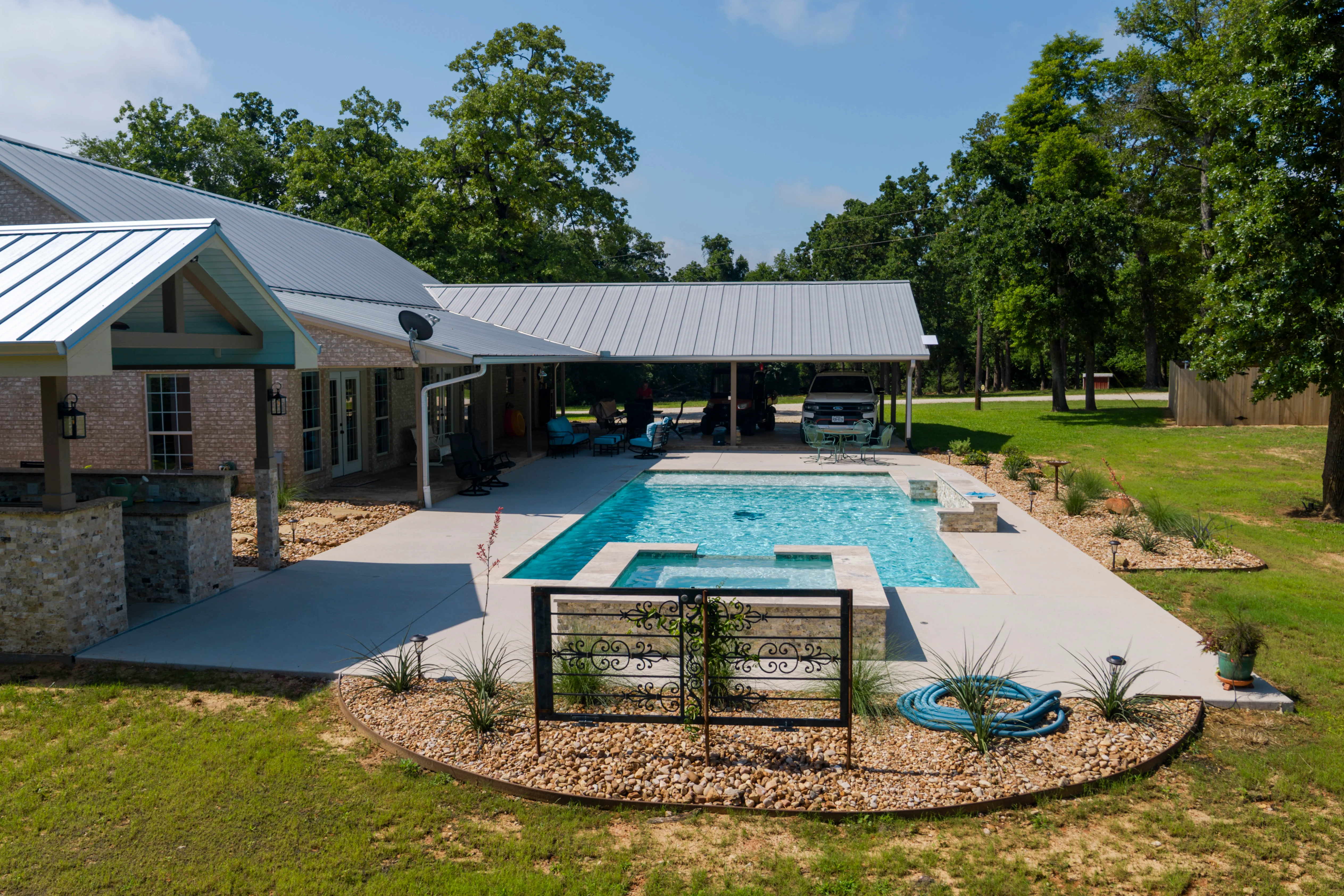 Modern pool and patio with metal gate, concrete deck, and landscaped grounds