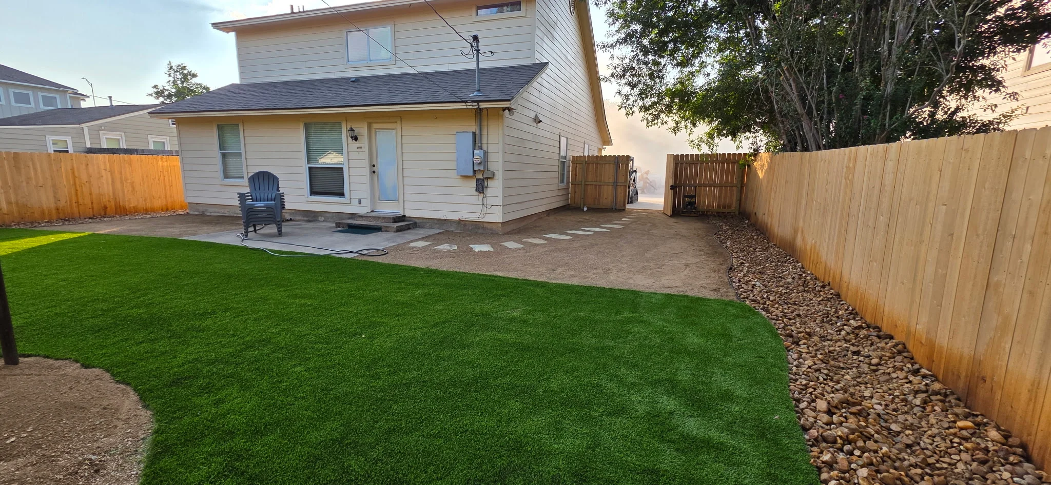 Residential backyard with synthetic grass, rock borders, concrete patio, and wood privacy fence