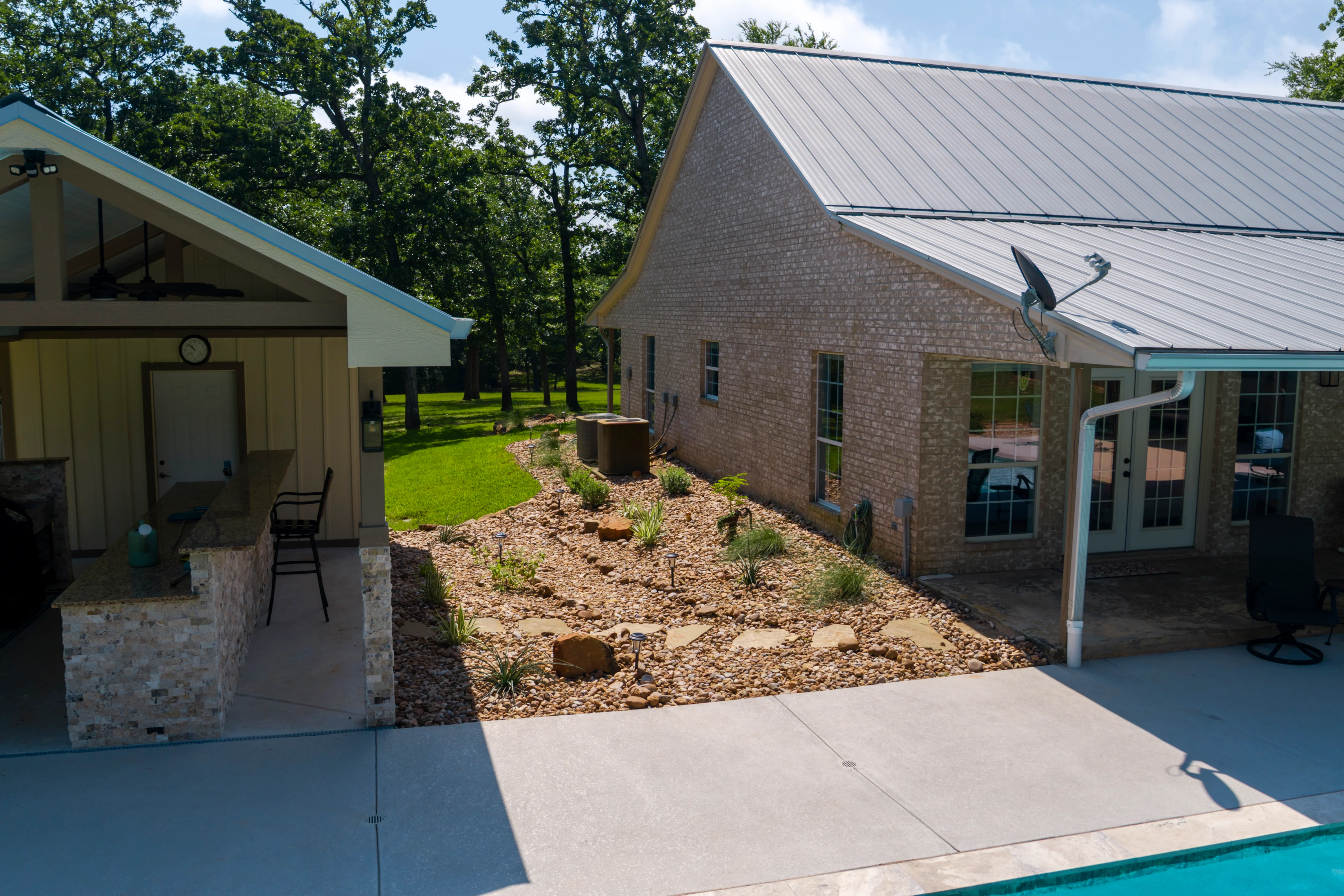 Residential backyard with river rock landscaping, native plants, and brick home with metal roof