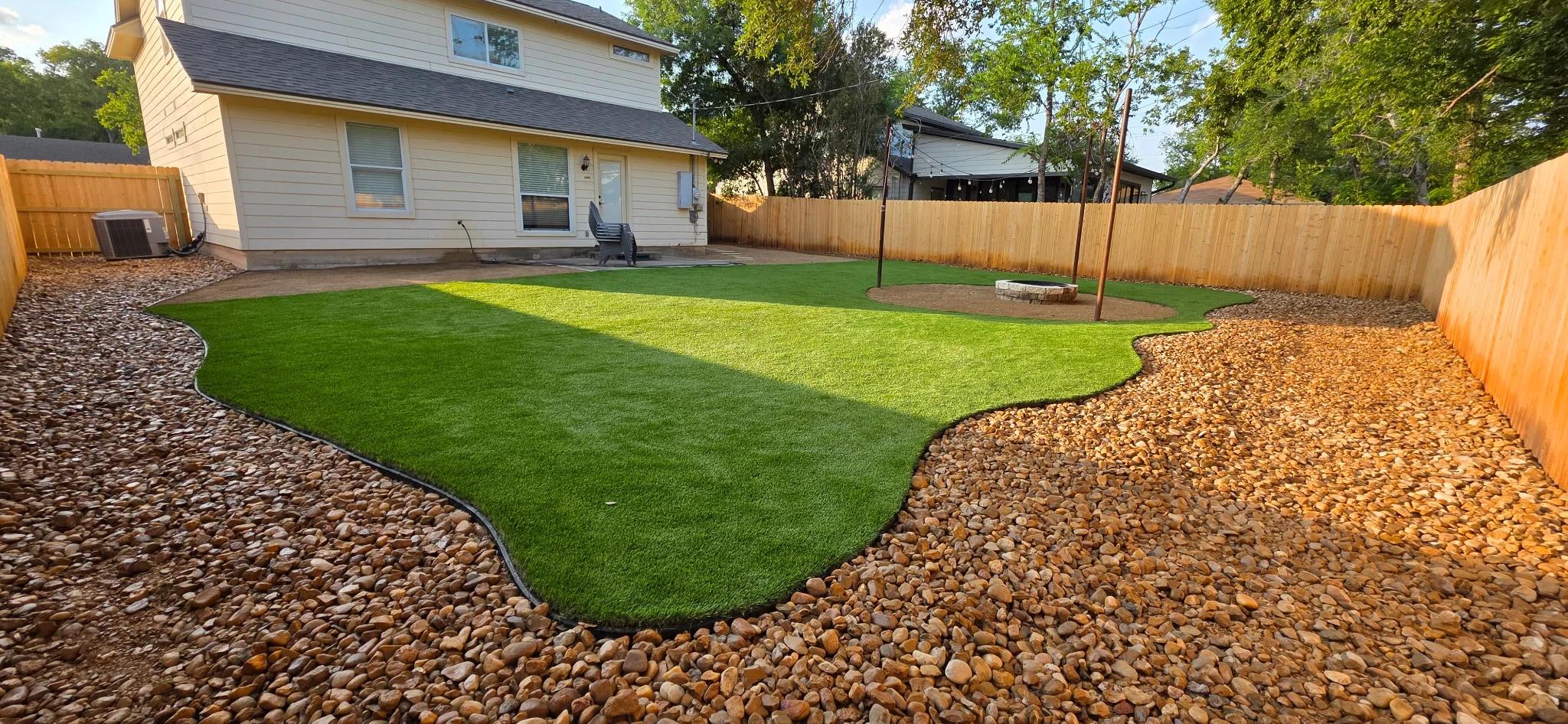 Backyard with synthetic grass, river rock borders, and wooden fence