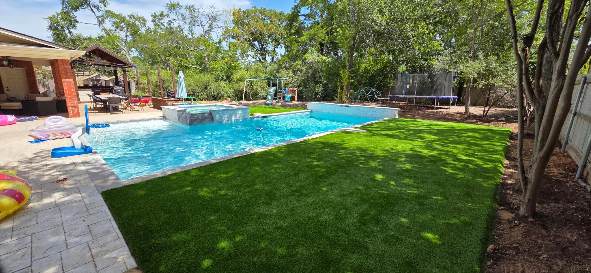 Sparkling blue swimming pool with spa, lush green lawn, and paver patio in residential backyard