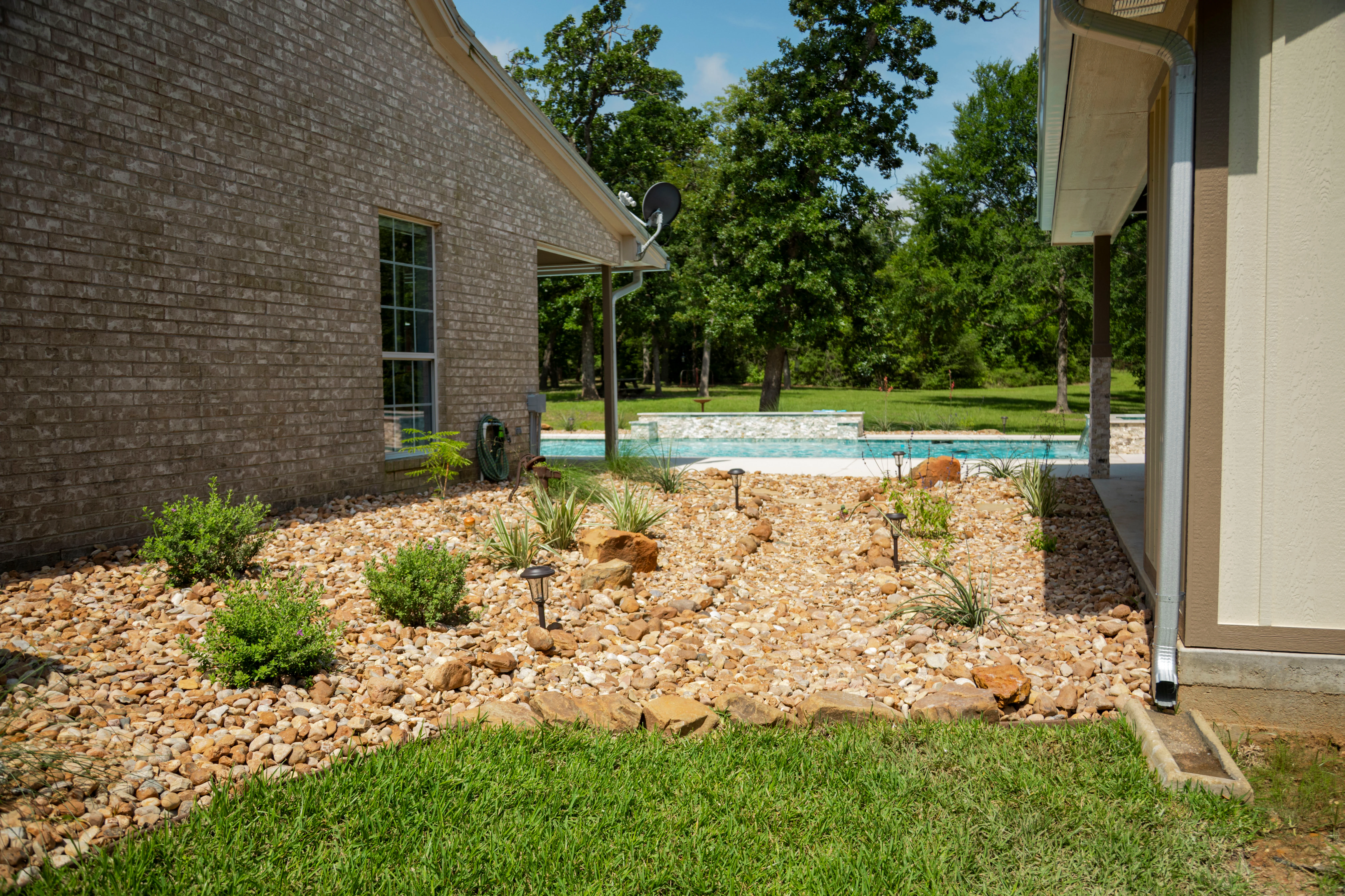 Xeriscaped courtyard with tan gravel, native plants, and solar lights beside brick home