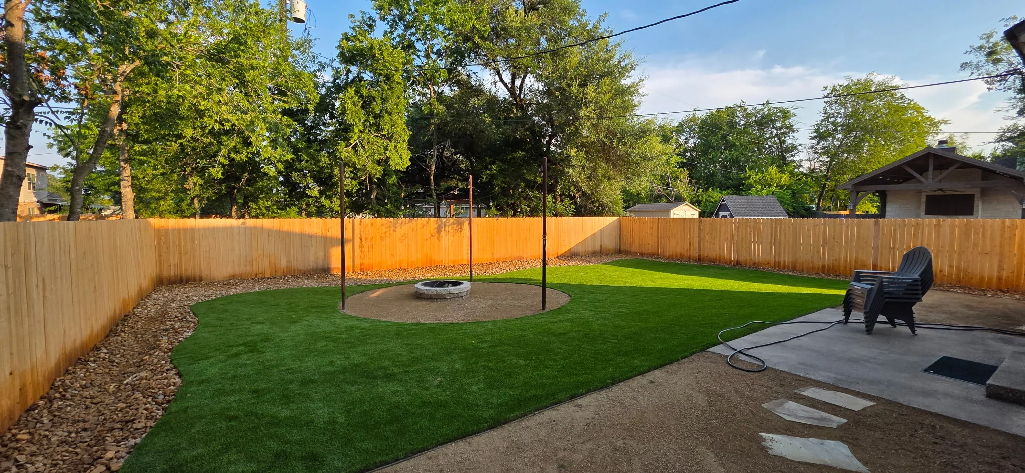 Backyard with synthetic grass, fire pit, cedar fence, and mature trees