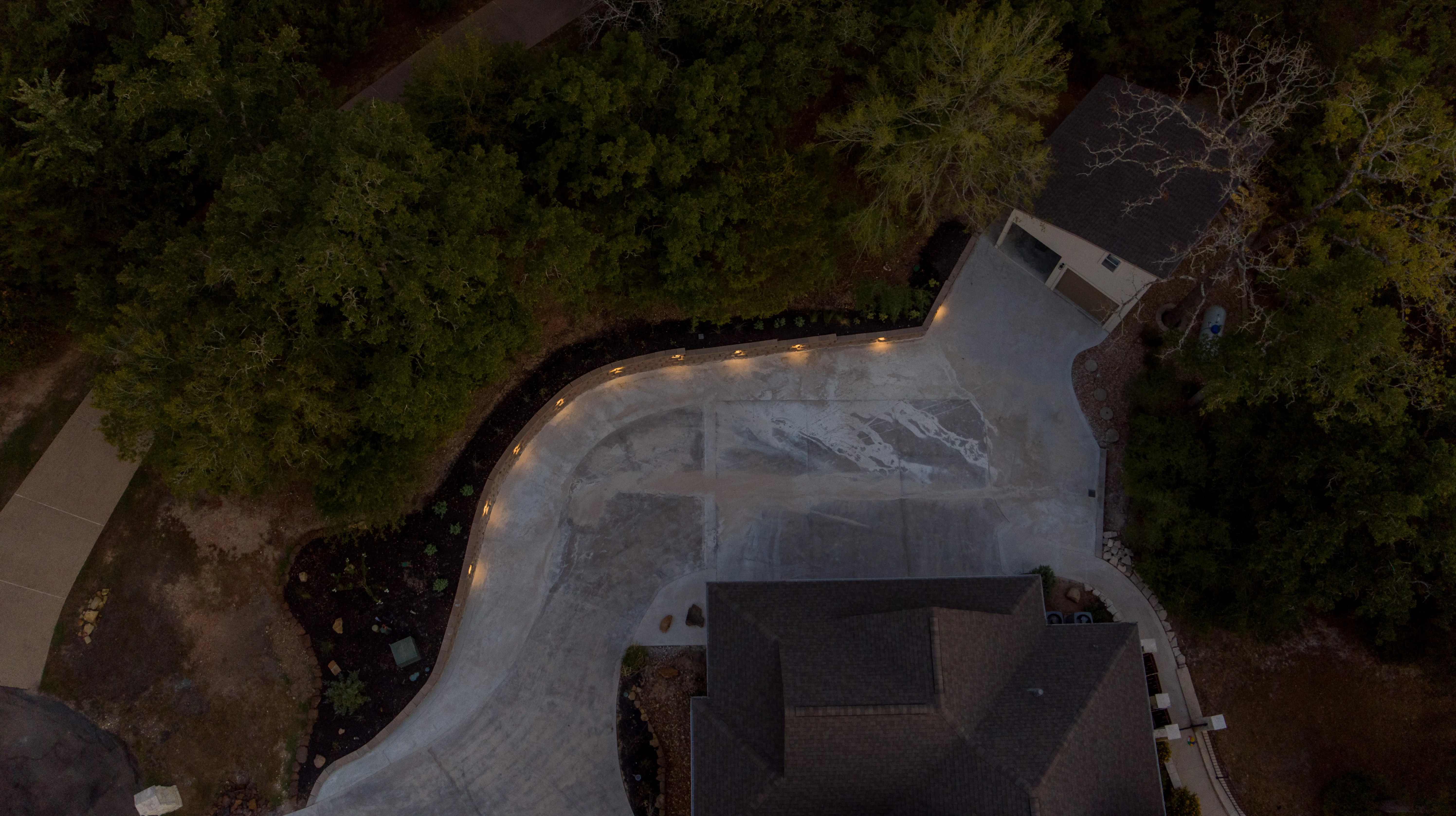 Aerial view of curved concrete driveway with edge lighting and mature trees